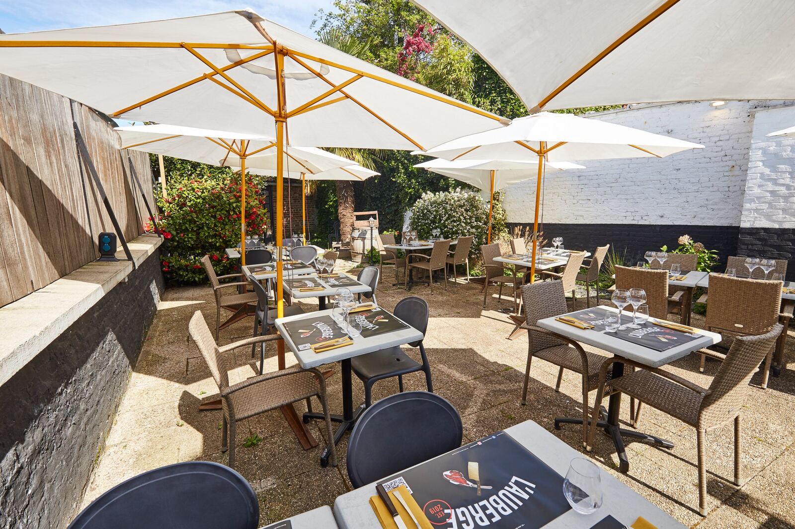 Les tables de la terrasse de L'Auberge de Mouvaux sous les parasols, au milieu des fleurs
